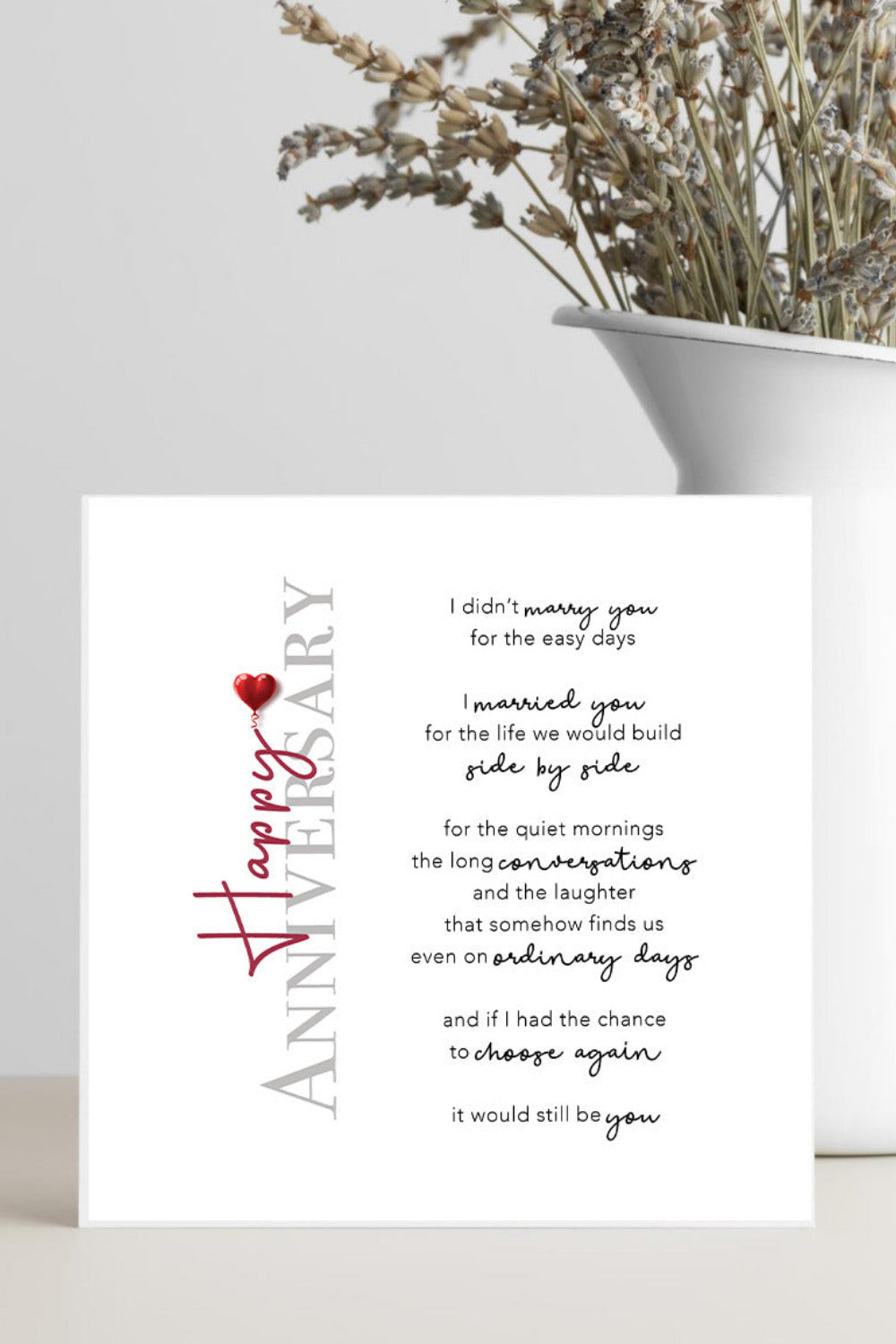Anniversary card with a heart design on a white surface with a vase of dried flowers.