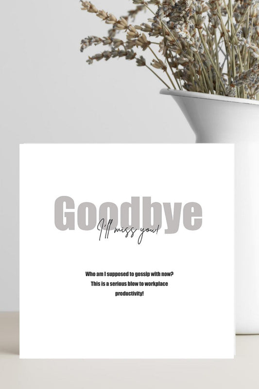 A white greeting card with the text 'Goodbye' and smaller farewell message, standing on a light surface beside a white vase filled with dried flowers against a light gray background.