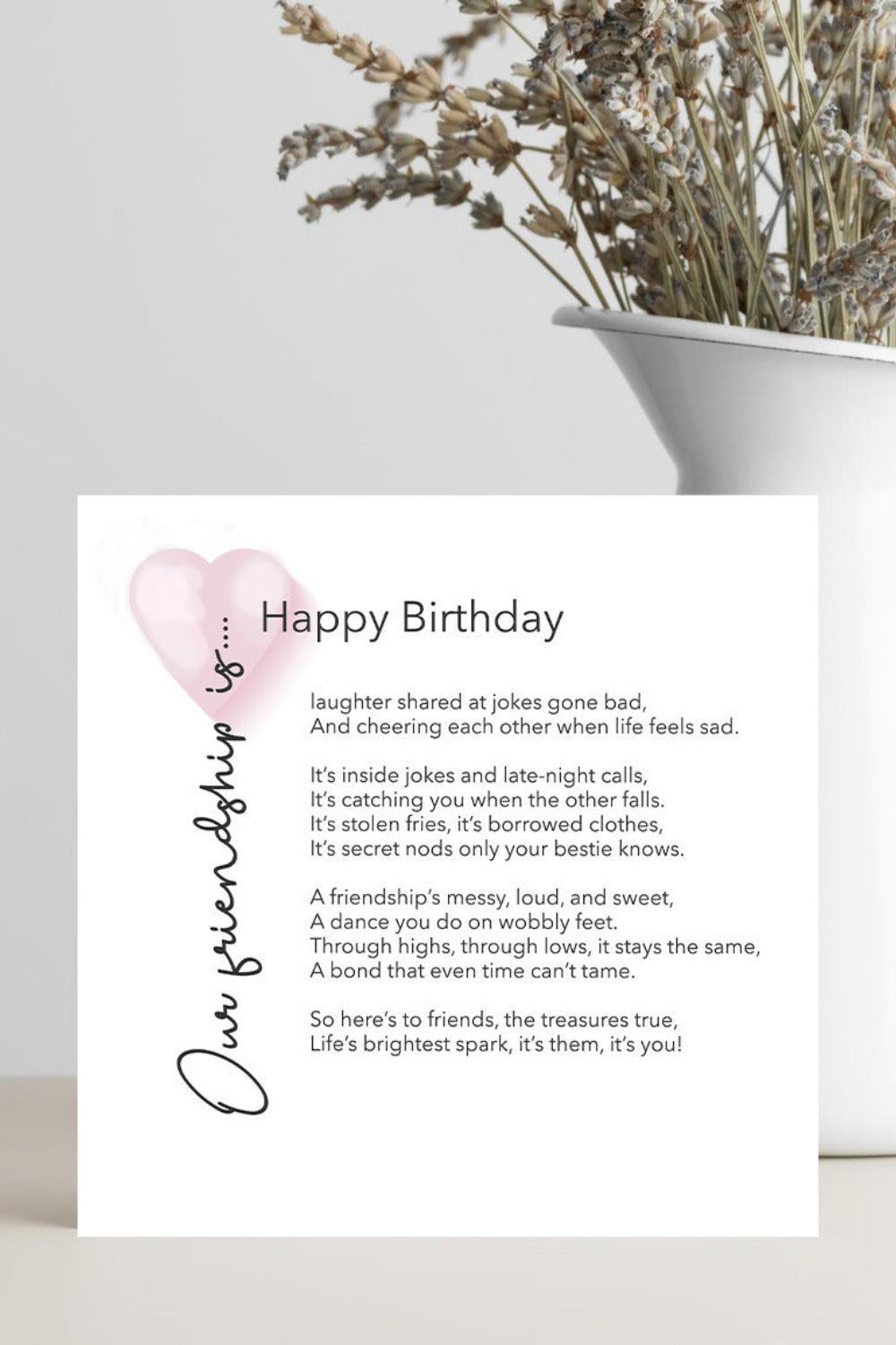 Greeting card with birthday message and heart design on a white surface with a plant in the background