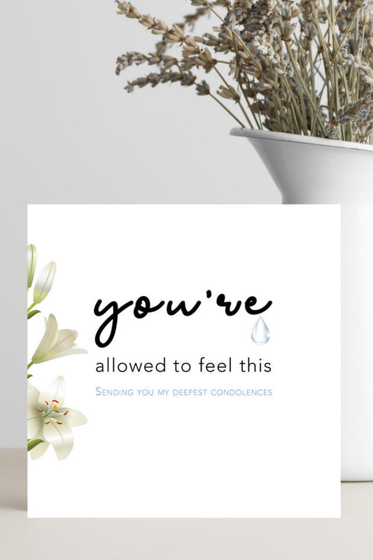 Greeting card with floral design and text on a white surface with a vase of flowers.