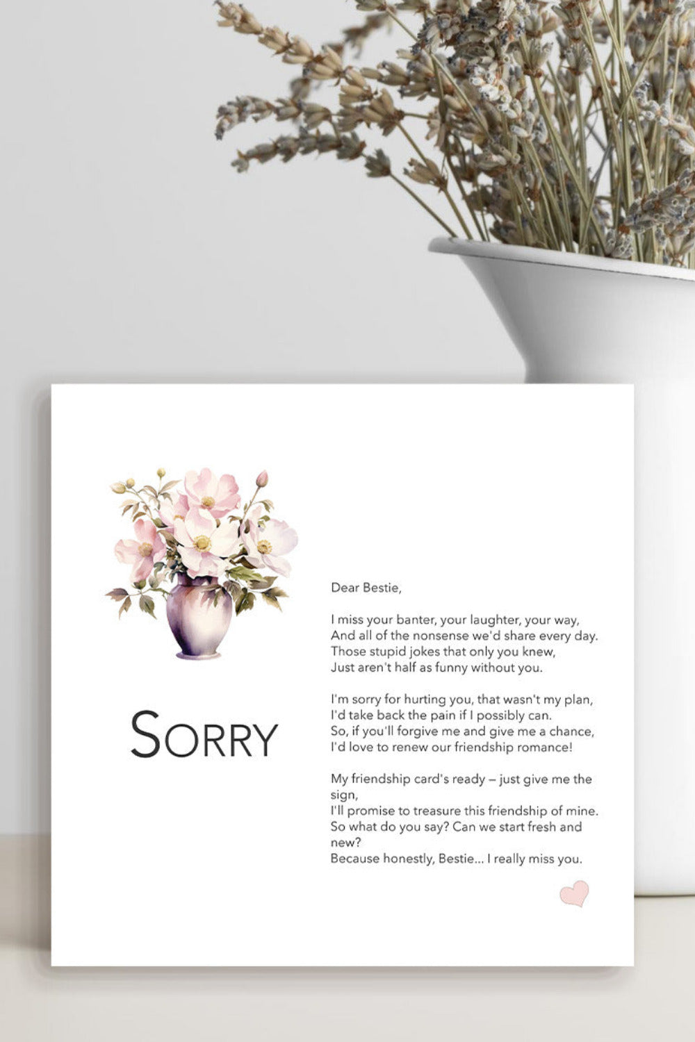 A printed sympathy card with a watercolor floral bouquet and the word 'Sorry' on a white background, styled on a light surface beside a white vase with dried flowers.