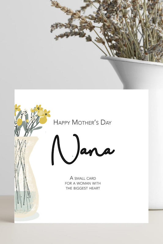 A square white greeting card with 'Happy Mother's Day Nana' printed in black script and serif text, plus a small floral illustration, standing in front of a white vase filled with dried flowers on a light neutral surface.