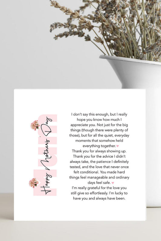 A square white card with a printed message for Mother's Day, styled in a flat-lay setting on a light gray surface next to a white pot containing dried plants.
