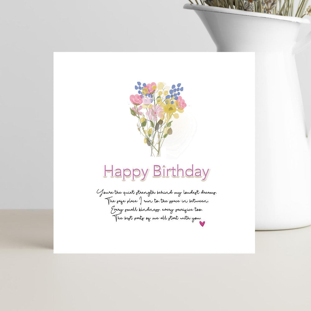 Greeting card with floral design and 'Happy Birthday' text on a white surface with a vase of dried flowers.