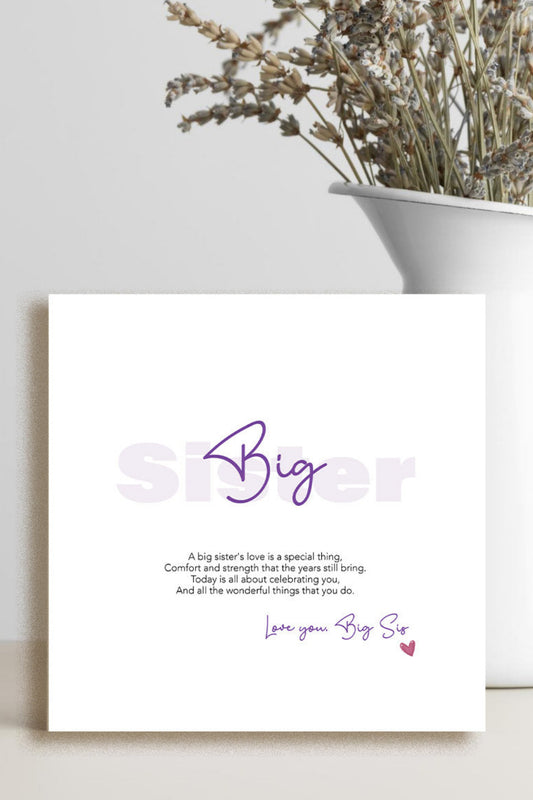 A square white greeting card with purple and black text reading 'Big Sister' and a short message, styled leaning against a light wall beside a white vase with dried flowers.