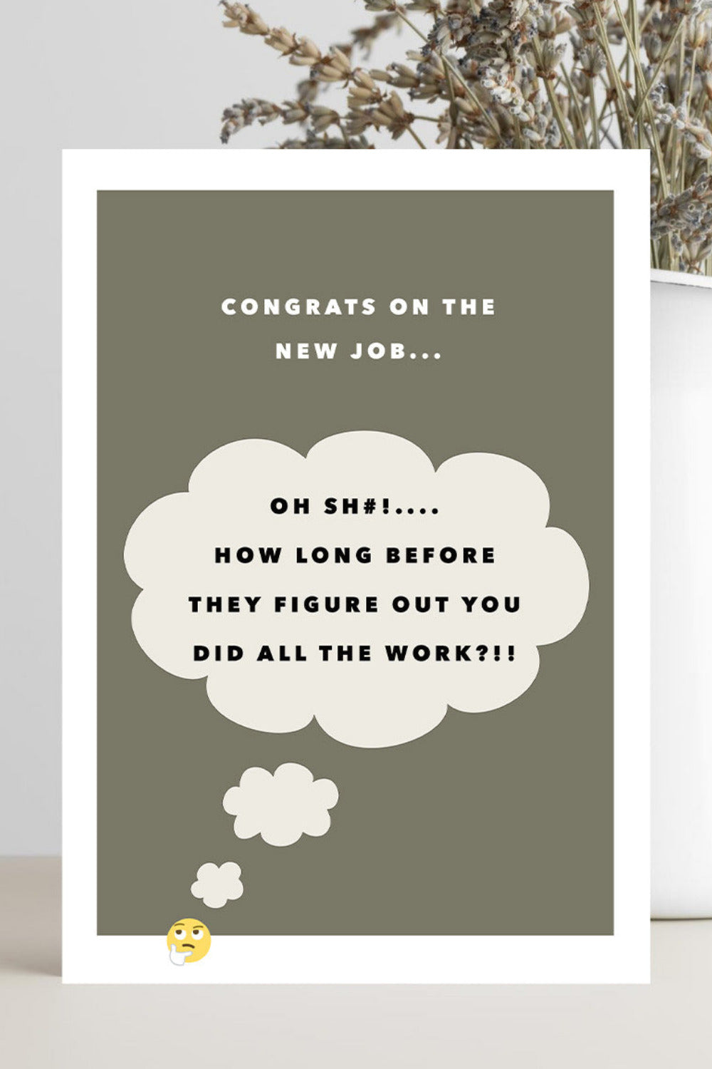 A rectangular congratulations card with a white border and a muted olive-gray background, placed on a light surface beside a white vase with dried flowers. The card reads: 'CONGRATS ON THE NEW JOB.