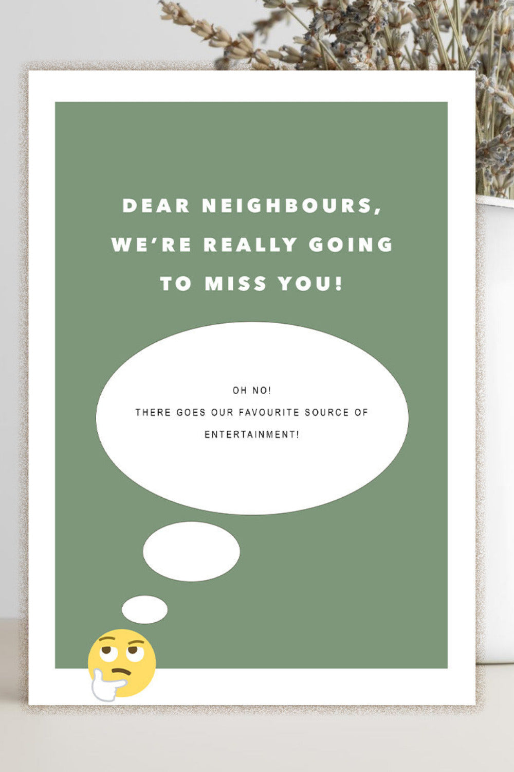 A rectangular greeting card with a sage green background and white border, printed with the text 'DEAR NEIGHBORS, WE'RE REALLY GOING TO MISS YOU!' and a thought bubble graphic. The card is photographed standing on a light surface beside a white vase with dried stems.