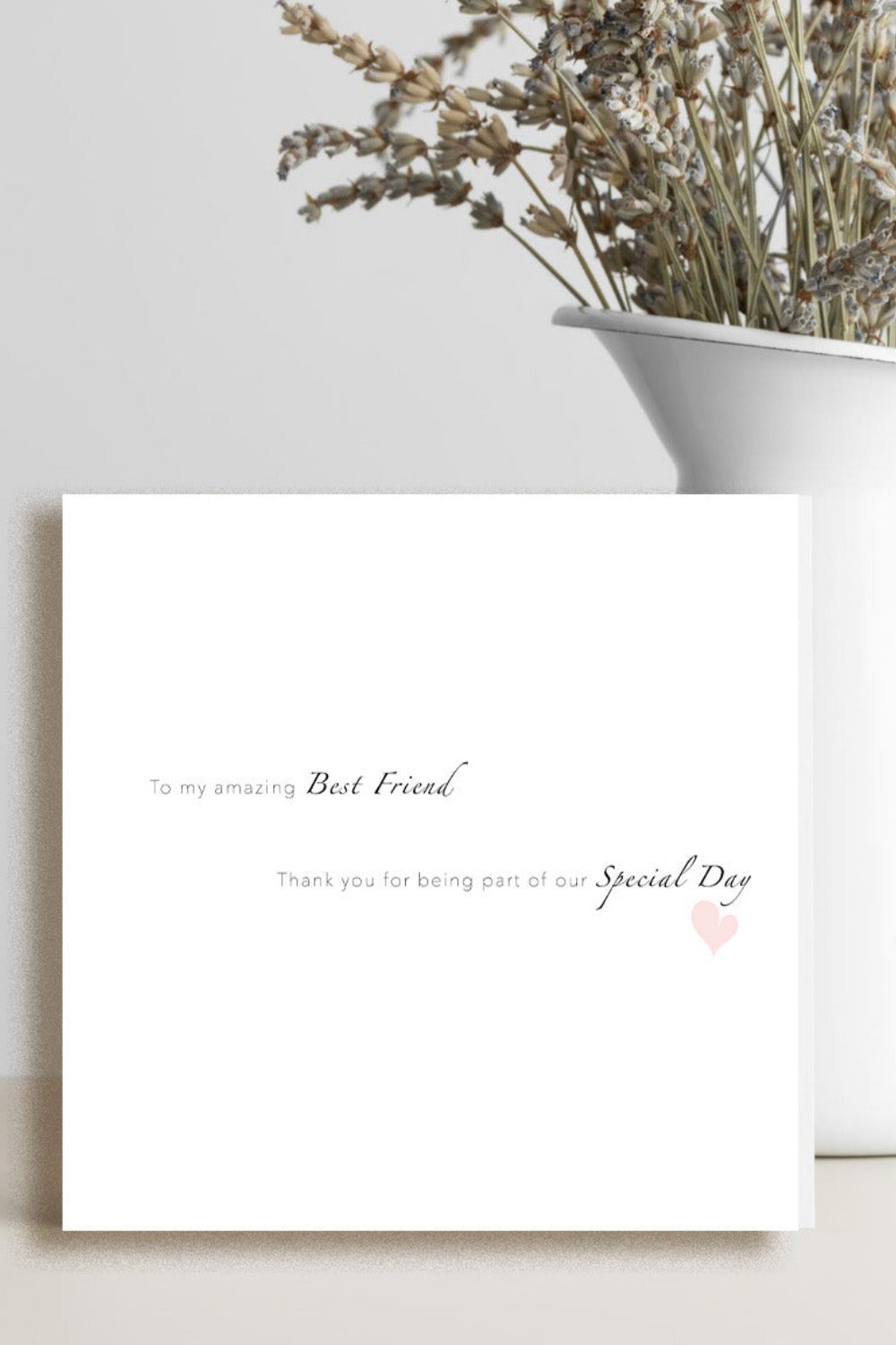 A white greeting card with delicate black script text and a small pink heart