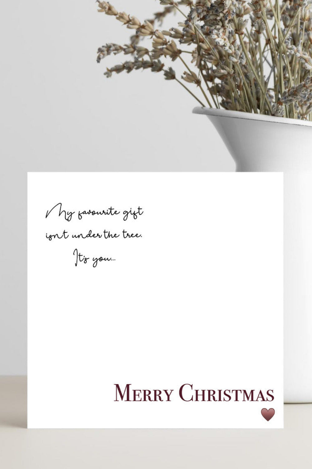 A white square Christmas greeting card with black script text reading 'My favorite gift isn't under the tree. For you.