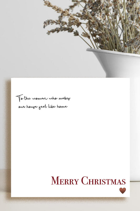 A square white Christmas greeting card with elegant black script text and 'Merry Christmas' in red serif font, styled on a light beige surface next to a white ceramic vase with dried flowers.