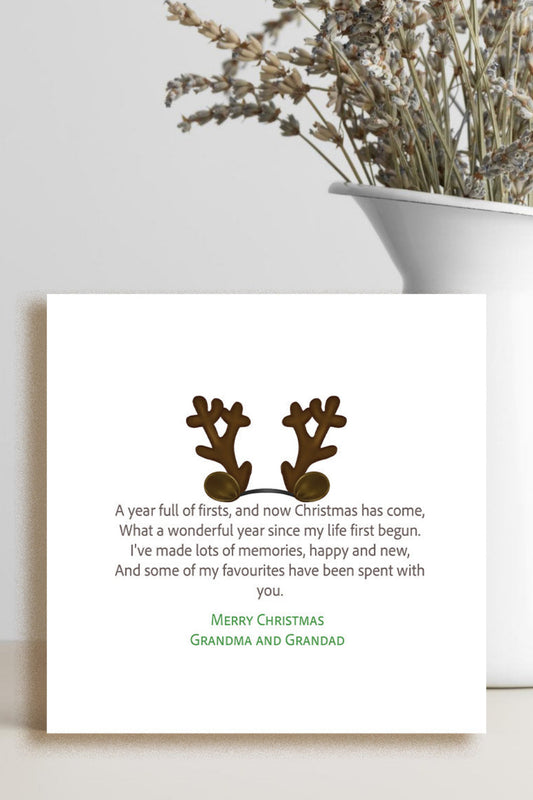 A square white Christmas greeting card with a poem and two brown reindeer antlers, styled on a light surface next to a white vase with dried flowers.