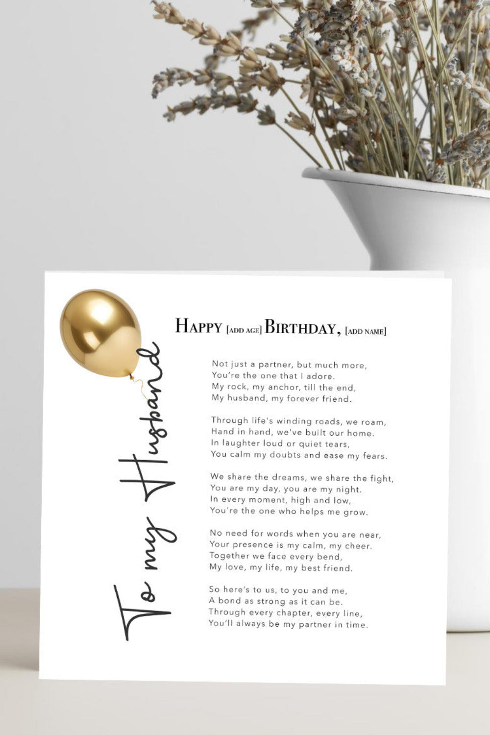 A square birthday card for a husband, featuring a poem and a gold foil balloon graphic, styled in a white vase with dried flowers on a light gray surface.