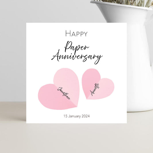 Personalised 1st wedding anniversary card with pink heart design, paper anniversary theme, customised with names and date.