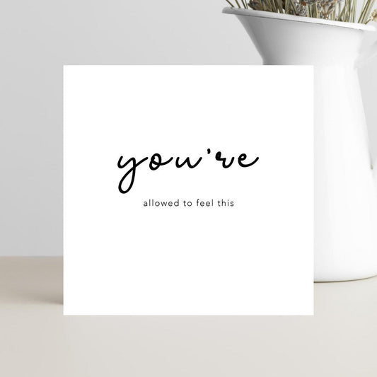 A minimalist condolence greeting card displaying the words “You’re Allowed to Feel This” in elegant script, placed on a soft neutral background conveying warmth, comfort, and understanding.