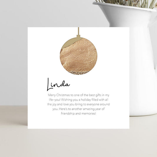 Greeting card with a gold ornament and Christmas message on white card.