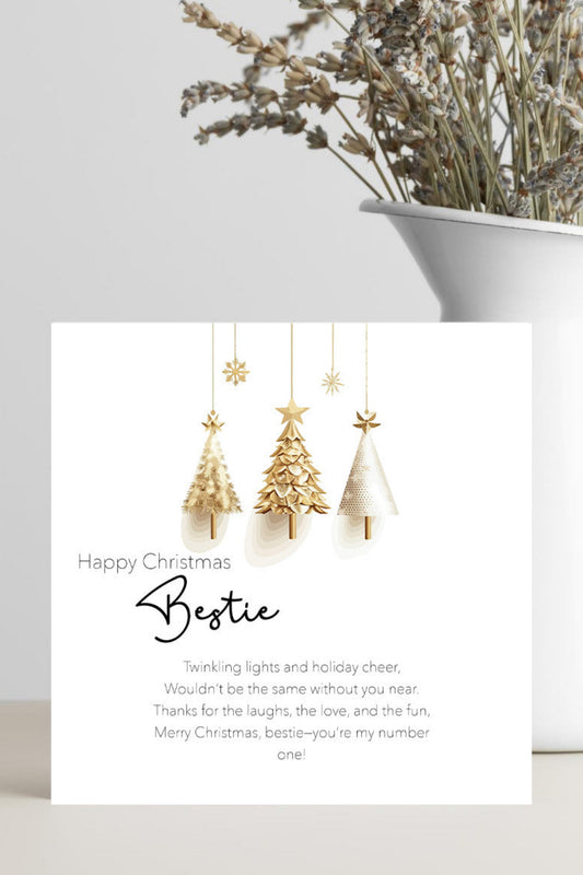 A white Christmas greeting card with gold and white hanging tree ornaments and a personalized poem, styled in a white ceramic vase with dried flowers against a light gray background.
